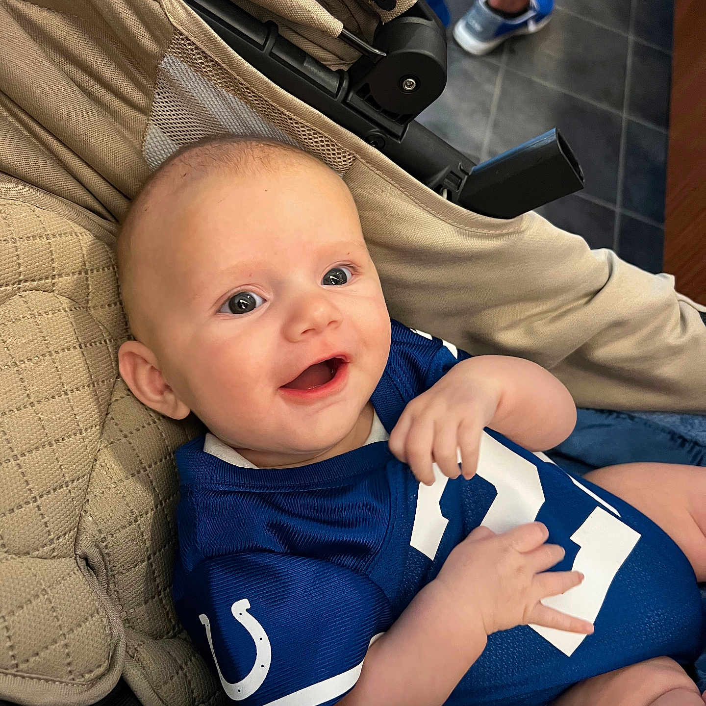 Axell joined the competition — help win amazing prizes! baby, child, infant, smiling, happy, portrait, stroller, football_uniform, sportswear, blue_clothing, indoors, tiled_floor, adult, legs, seated, reclining, close_up, face, family, photography
