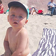 Youssef a rejoint le concours — aidez-le/la à gagner de superbes lots ! toddler, child, beach, sand, bucket, cap, sunny, outdoor, play, person, diaper, towel, relaxing, people, summer, blue_sky, wall, building, casual, daytime