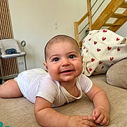 Ethan a rejoint le concours — aidez-le/la à gagner de superbes lots ! baby, infant, smiling, tummy, onesie, couch, heart_pillow, home_interior, wooden_stairs, drool, cute, child, indoors, furniture, happy, face, person, skin, hand, expression