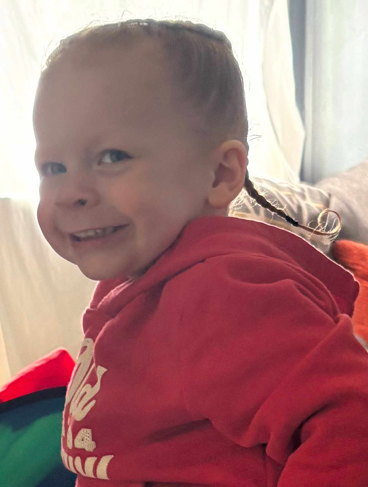 Jordan joined the competition — help win amazing prizes! child, smiling, braids, red_hoodie, indoors, natural_light, face, person, portrait, cute, happy, young, cozy, window_light, casual_clothing, playful, expression, head, cheeky, candid