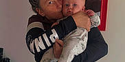 Jordan joined the competition — help win amazing prizes! baby, adult, hug, kiss, indoor, mirror, reflection, onesie, affection, person, portrait, face, clothing, glasses, hand, wall, table, object, casual, love