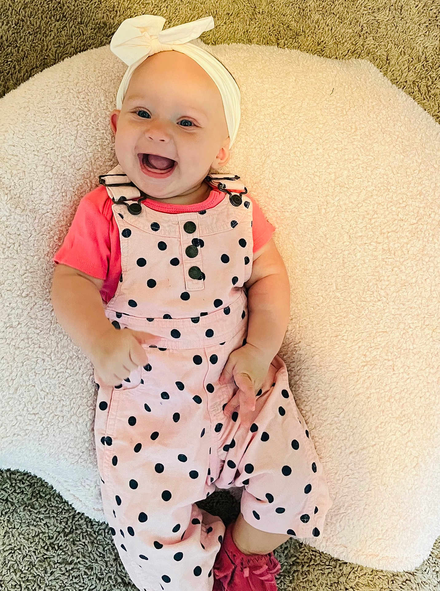 Laynie is registered to the contest to win money with this photo: baby, infant, smiling, headband, bow, pink_clothing, polka_dots, overalls, cushion, carpet, happy, child, cute, indoor, portrait, playful, feet, hands, fashion, toddler