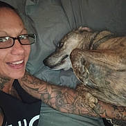 Buddy joined the competition — help win amazing prizes! animal, arm, bed, casual, closeup, comfort, dog, face, friendship, glasses, human, indoor, lying_down, person, pet, pillow, relaxed, rest, smile, tattoo