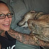 animal, arm, bed, casual, closeup, comfort, dog, face, friendship, glasses, human, indoor, lying_down, person, pet, pillow, relaxed, rest, smile, tattoo