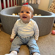 Ivy joined the competition — help win amazing prizes! baby, child, smiling, sitting, carpet, ball_pit, white_shirt, jeans, sneakers, red_bow, indoor, playroom, happy, cute, person, footwear, toy_balls, floor, young_child, portrait