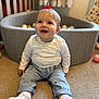 baby, child, smiling, sitting, carpet, ball_pit, white_shirt, jeans, sneakers, red_bow, indoor, playroom, happy, cute, person, footwear, toy_balls, floor, young_child, portrait