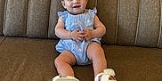 Ivy joined the competition — help win amazing prizes! baby, blue_bow, brown_sofa, casual_clothing, child, comfortable, cute, furniture, happy, indoor, infant, one_person, portrait, romper, sitting, smiling, sofa, white_sandals, wood_paneling, young_child
