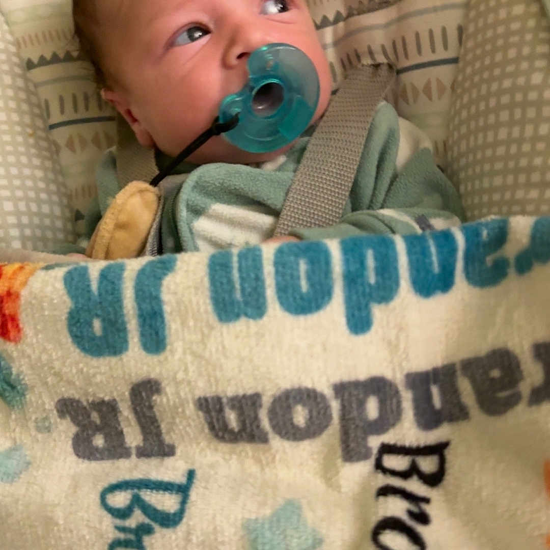 Brandon Jr joined the competition — help win amazing prizes! baby, bed, blanket, blue, child, closeup, comfort, cute, fabric, face, indoors, infant, pacifier, pattern, person, sleeping_bag, soft, text, wrapped, young