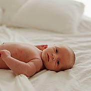 Banx is registered to the contest to win money with this photo: baby, newborn, infant, lying_down, bed, pillow, soft_light, skin, face, eyes, curious, peaceful, indoors, blanket, resting, human, child, portrait, sleepwear, comfortable