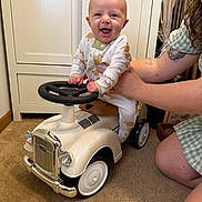Banx joined the competition — help win amazing prizes! baby, child, toy_car, indoor, car, smile, person, pajamas, hand, carpet, furniture, cabinet, adult, supporting, happy, steering_wheel, vintage, playtime, cute, tattoo
