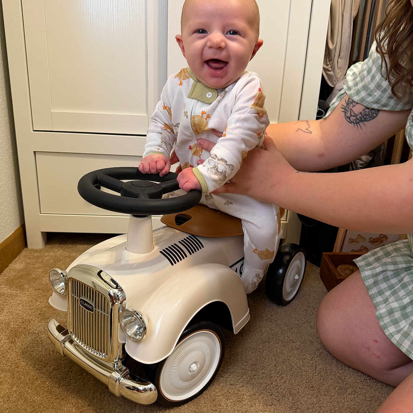 Banx joined the competition — help win amazing prizes! baby, child, toy_car, indoor, car, smile, person, pajamas, hand, carpet, furniture, cabinet, adult, supporting, happy, steering_wheel, vintage, playtime, cute, tattoo
