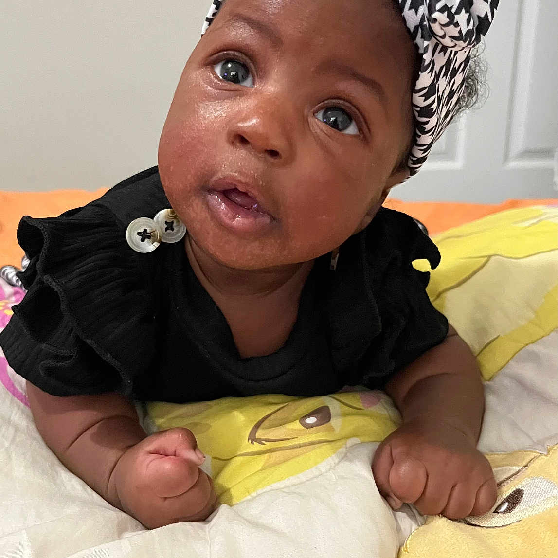 Sharlette is registered to the contest to win money with this photo: baby, infant, headband, black_clothing, blanket, cartoon, cute, face, portrait, child, indoor, skin, hands, expression, lying_down, young, adorable, curious, colorful, soft