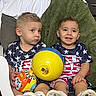 american_flag, ball, blue, chair, child, cushion, footwear, happy, indoor, matching_clothes, orange, person, playing, short_hair, sitting, smiling, stars, toddler, toy, yellow