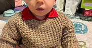 Jaxon is registered to the contest to win money with this photo: beige_pants, blanket, casual_clothing, child, curious, expression, floor, furniture, gifts, home, indoor, knitted_sweater, pattern, person, remote_control, seated, toddler, toys, window, young_child