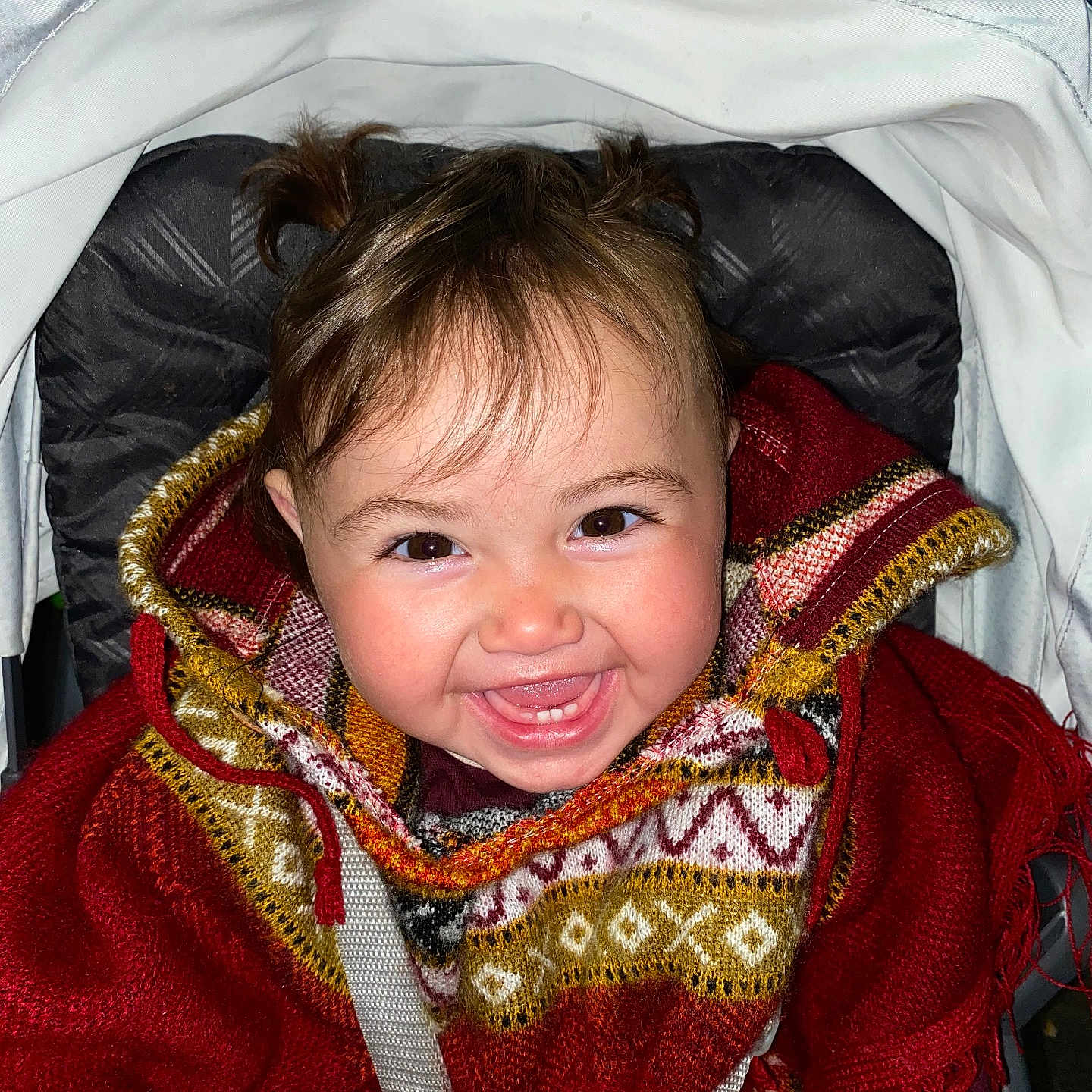 Narielis joined the competition — help win amazing prizes! baby, brown_hair, child, child_seat, clothing, cute, face, hair, happy, indoors, infant, patterned_clothing, poncho, portrait, red, seatbelt, smile, stroller, toddler, warm_clothing