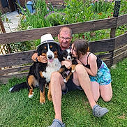 Vasko a rejoint le concours — aidez-le/la à gagner de superbes lots ! bernese_mountain_dog, casual_clothing, dog, family, flowers, footwear, garden, girl, glasses, grass, happy, hat, man, nature, outdoor, pet, puppy, smiling, summer, wooden_fence