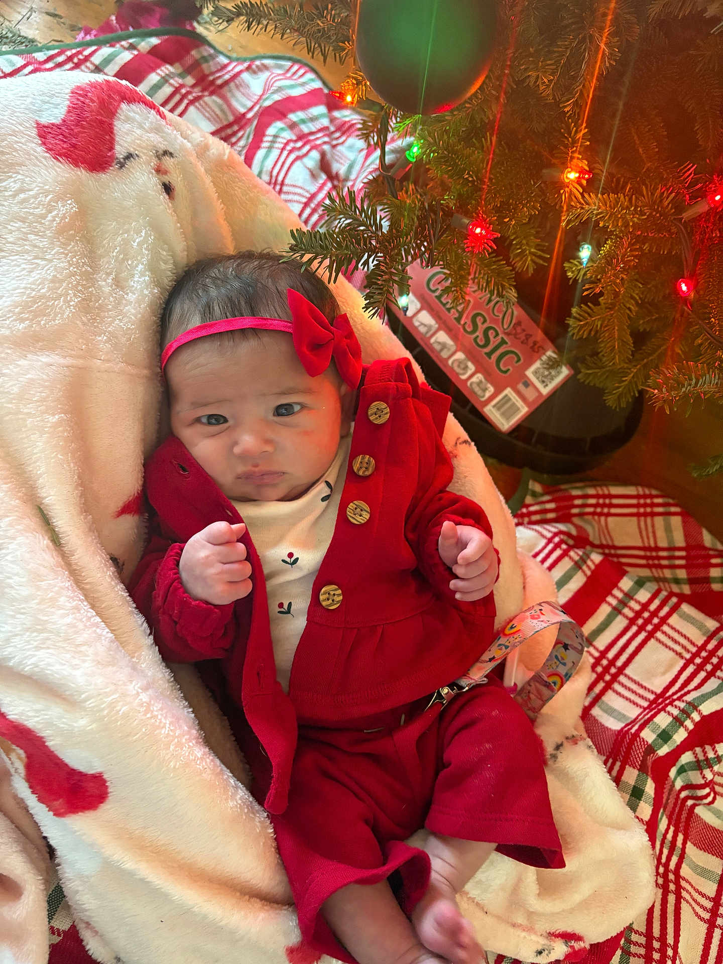 Vivianne is registered to the contest to win money with this photo: baby, infant, red_clothing, headband, blanket, christmas_tree, christmas_lights, plaid, floor, wood_floor, holiday, decorations, cute, indoors, person, newborn, festive, cozy, wrapped, relaxing