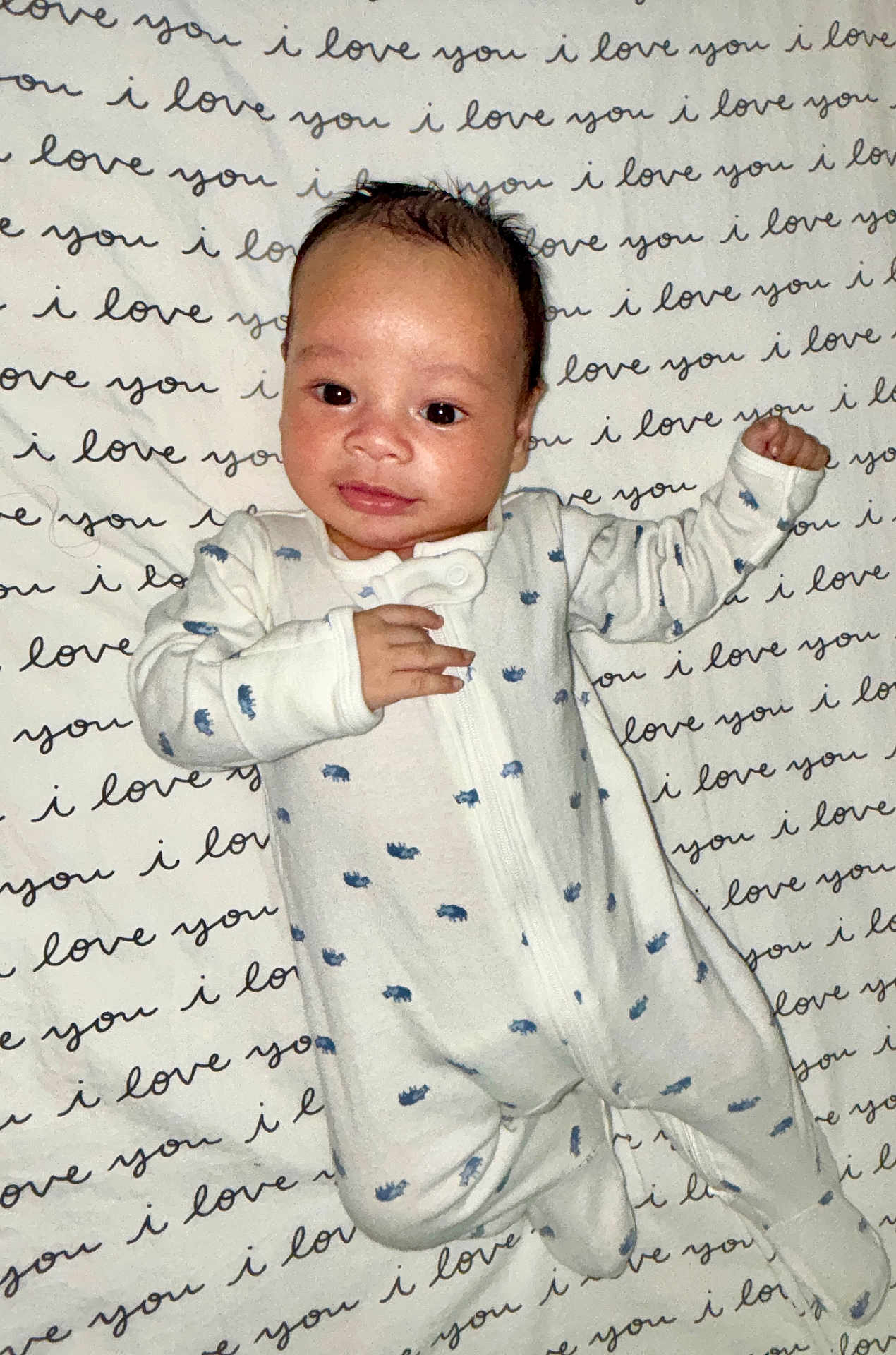 Noah is registered to the contest to win money with this photo: baby, infant, onesie, blanket, text_pattern, love_message, sleepwear, cute, portrait, child, newborn, lying_down, smiling, face, hands, feet, cozy, indoor, closeup, adorable