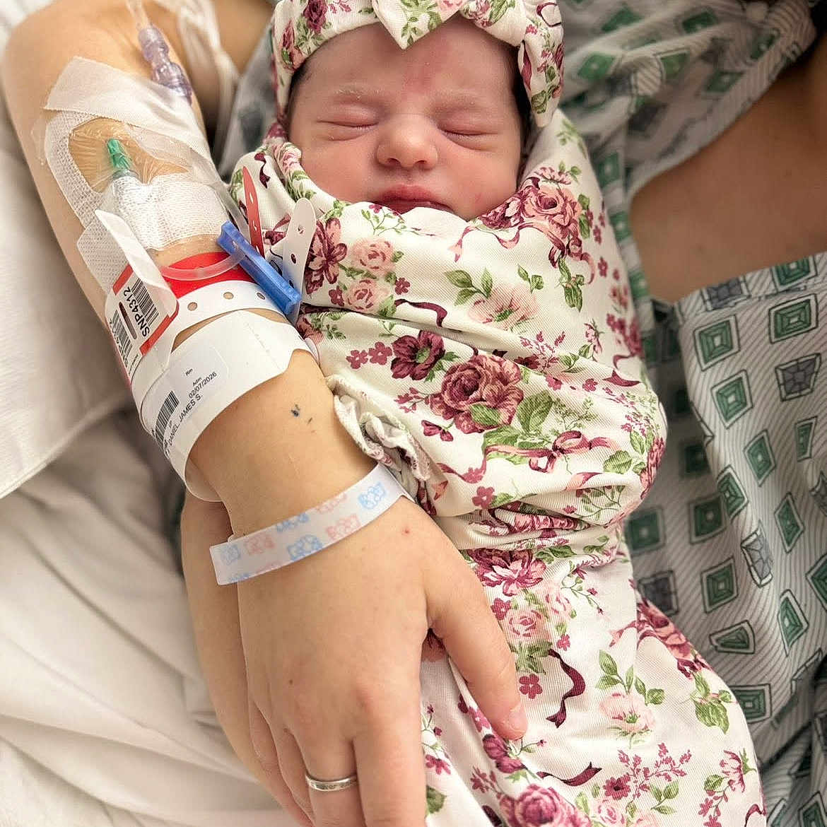 Amberley is registered to the contest to win money with this photo: baby, bed, closeup, floral_pattern, gown, hand, headband, hospital, hospital_room, infant, iv_line, mother, newborn, parent, peaceful, skin, sleeping, swaddled, wedding_ring, wristband
