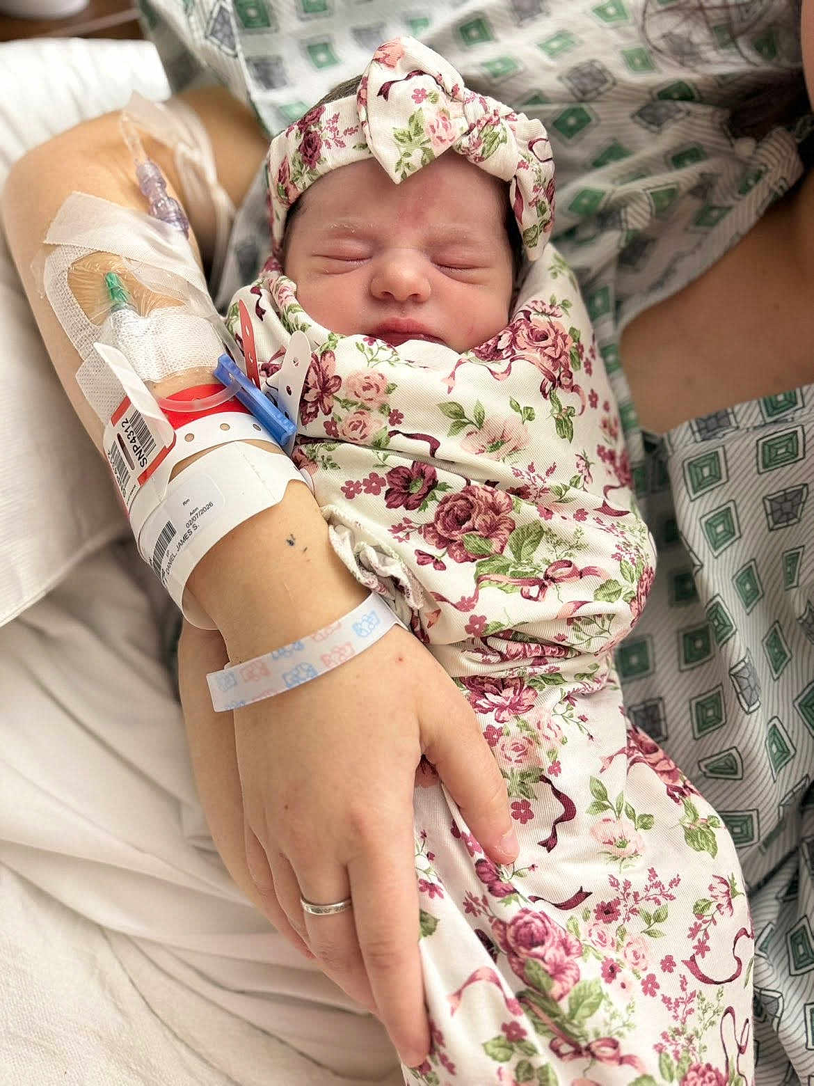 Amberley is registered to the contest to win money with this photo: newborn, baby, infant, swaddled, floral_pattern, headband, sleeping, hospital, hospital_room, iv_line, wristband, hand, wedding_ring, parent, mother, gown, closeup, skin, bed, peaceful