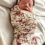baby, newborn, swaddle, blanket, floral_pattern, headband, sleeping, closed_eyes, peaceful, portrait, indoor, bed, bedding, fabric, clothing, infant, cute, pink, soft_texture, wrapped