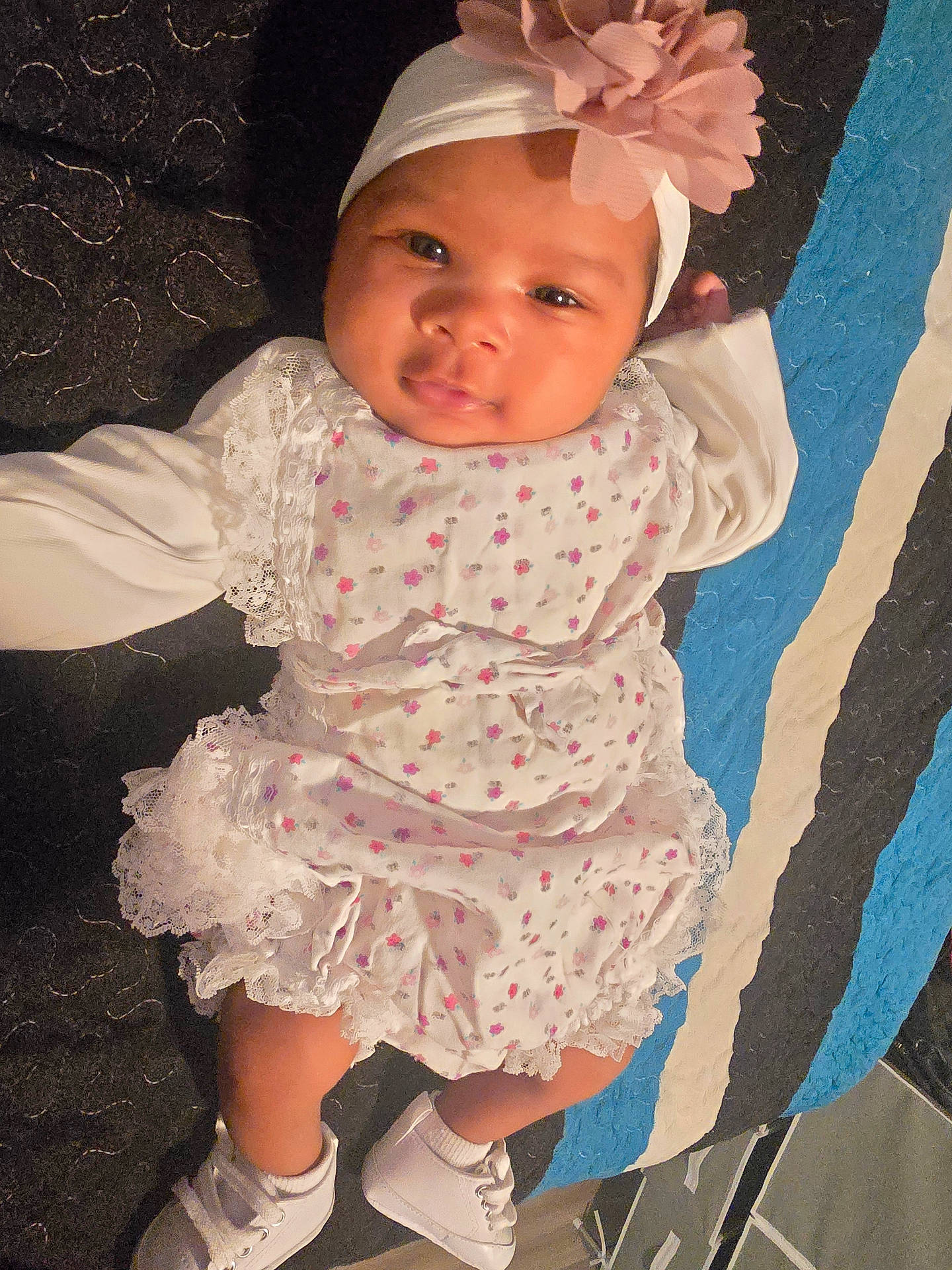 Arisbeth is registered to the contest to win money with this photo: adorable, baby, carpet, child, cute, dress, face, flower, headband, indoor, infant, lying_down, person, portrait, shoes, smile, socks, striped_background, white_clothing, young
