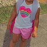 Kennedi is registered to the contest to win money with this photo: child, girl, backpack, shorts, shirt, heart, outdoor, sidewalk, grass, plants, shoes, smile, sunlight, summer, cute, fashion, portrait, standing, happy, beads