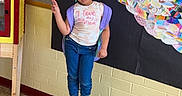 Kennedi joined the competition — help win amazing prizes! child, girl, stool, library, colorful_art, paper_feathers, peace_sign, playful, pouty_face, hair_beads, wall_art, bulletin_board, floor, jeans, sneakers, tshirt, indoor, school, hallway, expression