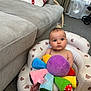 baby, inflatable_seat, plush_toy, colorful, living_room, couch, blanket, teddy_bear_pattern, carpet, window, curtains, baby_stroller, toy, child, infant, foot, face, person, indoor, furniture