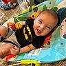 baby, infant, child, smiling, happy, portrait, sitting, activity_seat, baby_toy, plush_toy, colorful, indoor, nursery, crib, carpet, clothing, black_shirt, gray_shorts, playtime, close_up