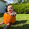 Oliver is registered to the contest to win money with this photo: baby, child, pumpkin, halloween, costume, outdoor, grass, garden, backyard, smiling, happy, sitting, portrait, sunlight, nature, greenery, striped_shirt, socks, infant, seasonal