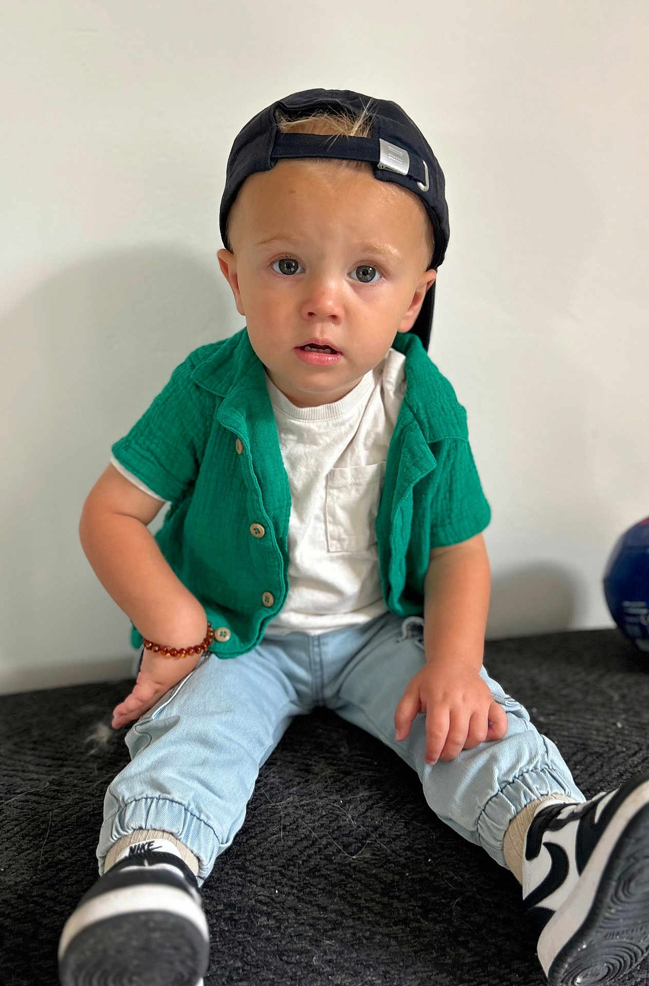 Abel a rejoint le concours — aidez-le/la à gagner de superbes lots ! toddler, child, sitting, green_shirt, white_tshirt, blue_pants, black_cap, bracelet, sneakers, nike, indoor, curious, portrait, young_child, casual_clothing, black_and_white, expression, cute, fashion, person