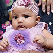 Jiyana is registered to the contest to win money with this photo: baby, child, infant, pink_headband, flower_accessory, purple_tulle, hands, adult_hands, dress, closeup, portrait, outdoor, face, cute, person, skin, expression, soft_light, colorful_background, fabric