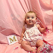 Molina is registered to the contest to win money with this photo: baby, infant, child, pink_backdrop, romper, sitting, smile, face, confetti, shredded_paper, card, letter_m, toes, legs, studio_shot, portrait, cheeks, decor, fabric, cute