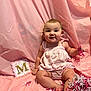 baby, infant, child, pink_backdrop, confetti, decorative_card, letter_m, pink_dress, sitting, smiling, portrait, fabric, shredded_paper, toes, chubby_cheeks, big_eyes, hand, celebration, studio_setup, cute