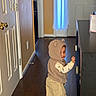 baby_shoes, beige_clothing, cabinet, candid, cargo_pants, child, countertop, cozy, curtain, door, glance, hallway, hand_on_cabinet, hardwood_floor, home_interior, hooded_vest, indoor, smile, standing, toddler