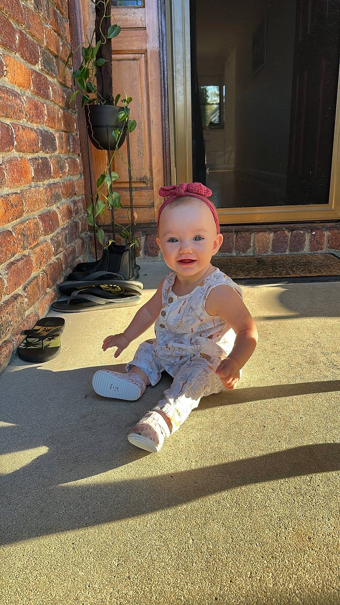 Patience joined the competition — help win amazing prizes! asphalt, baby, baby_toddler_clothing, child, floor, flooring, flowerpot, grass, happy, houseplant, human_leg, leisure, person, plant, road_surface, sidewalk, sitting, smile, toddler, window
