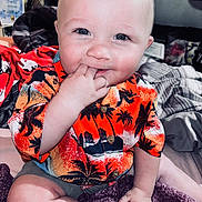 Wyatt joined the competition — help win amazing prizes! baby, child, infant, smiling, sitting, hand_in_mouth, orange_shirt, hawaiian_shirt, patterned_clothing, shorts, indoor, blanket, bed, cute, happy, portrait, face, blue_eyes, light_skin, playful