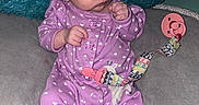 Delilah is registered to the contest to win money with this photo: baby, infant, child, portrait, sitting, purple_onesie, hearts, pacifier, pacifier_clip, cushion, pillow, blue_pillow, indoor, home, wide_eyed, hands, baby_clothing, soft_furnishings, close_up, adorable