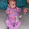 baby, infant, child, portrait, sitting, purple_onesie, hearts, pacifier, pacifier_clip, cushion, pillow, blue_pillow, indoor, home, wide_eyed, hands, baby_clothing, soft_furnishings, close_up, adorable