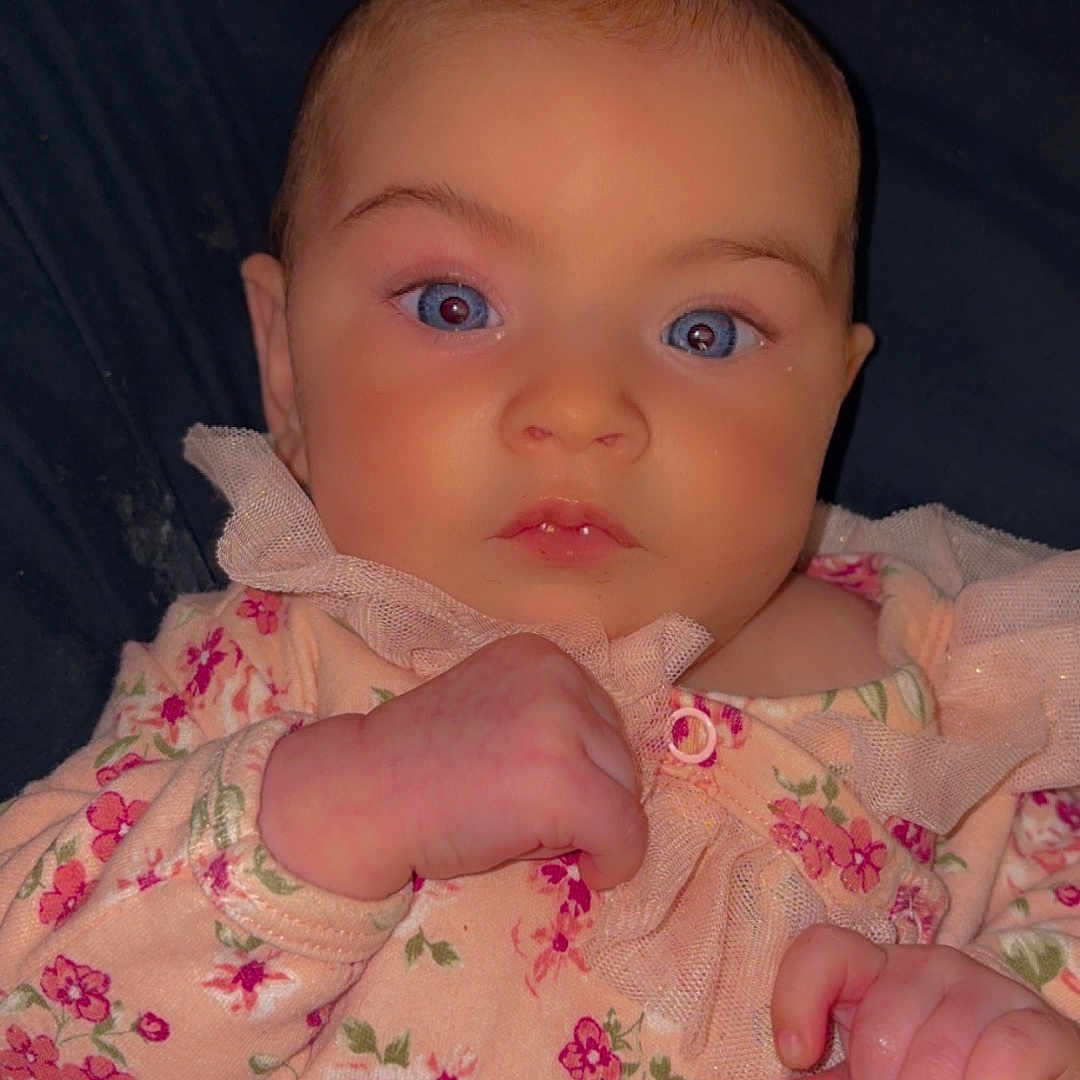 Delilah is registered to the contest to win money with this photo: baby, infant, child, portrait, lying_down, floral_outfit, dress, wide_eyes, face, hands, rosy_cheeks, indoor, blanket, close_up, front_facing, looking_at_camera, cute, calm, photography, headshot