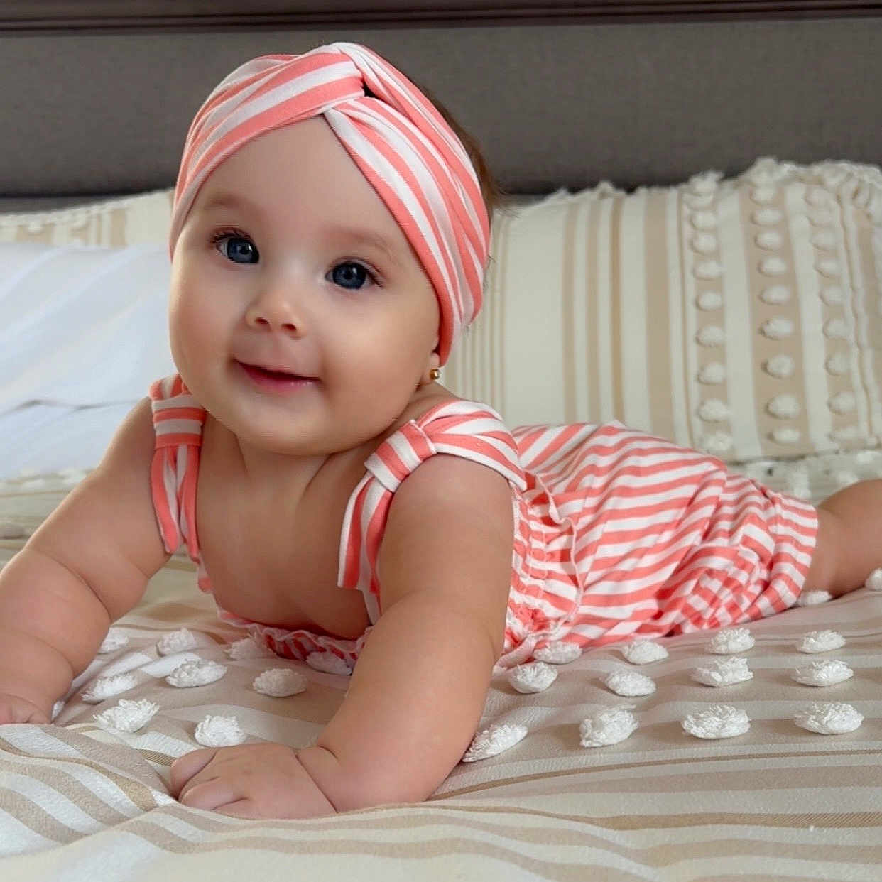 Adaiah is registered to the contest to win money with this photo: apparel, baby, bed, child, crawling, cute, face, happy, headband, indoors, infant, lying_down, person, pillow, portrait, skin, smile, striped_clothing, toddler, young