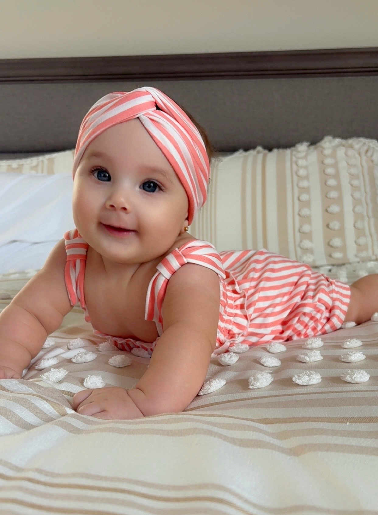 Adaiah is registered to the contest to win money with this photo: baby, child, portrait, smile, headband, striped_clothing, bed, pillow, crawling, cute, infant, happy, person, skin, indoors, apparel, lying_down, face, young, toddler