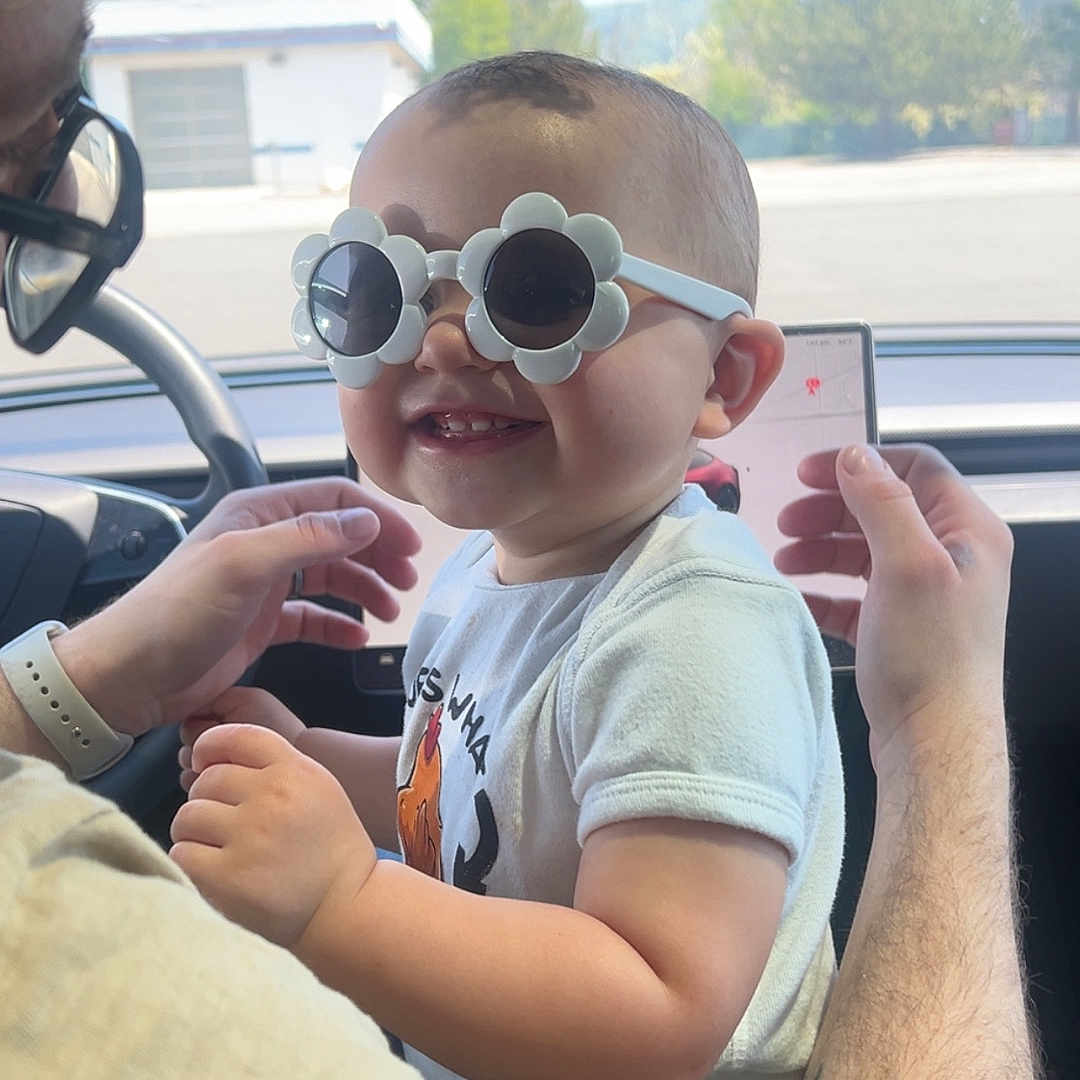 Lonna Valerie joined the competition — help win amazing prizes! adult, baby, car_interior, child, dashboard, daylight, flower_shaped_glasses, hands, happy, person, rearview_mirror, road, seat, short_hair, smile, sunglasses, tattoo, vehicle, white_shirt, window