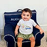 Augustine joined the competition — help win amazing prizes! toddler, child, smiling, chair, navy_blue, tshirt, shorts, camo, barefoot, carpet, indoor, person, young_child, happy, seated, furniture, home, casual_clothing, portrait, cute