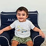 Augustine is registered to the contest to win money with this photo: toddler, child, smiling, sitting, armchair, clothing, white_tshirt, camo_shorts, indoor, carpet, happy, person, face, feet, hair, background_wall, furniture, cute, young_child, relaxed