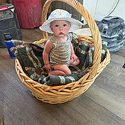 Jane joined the competition — help win amazing prizes! baby, basket, hat, quilt, indoor, wood_floor, child, wicker, curious, blue_eyes, sitting, plaid, blanket, face, person, floor, cabinet, red_bin, tool, expression
