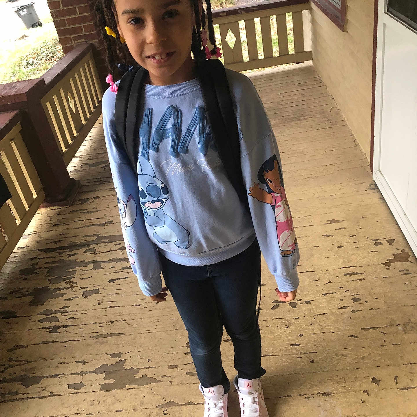 Maliyah joined the competition — help win amazing prizes! backpack, beads, braids, casual_clothing, child, daylight, door, girl, house, jeans, outdoor, person, porch, railing, smiling, sneakers, standing, sweatshirt, window, wooden_floor