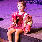 Alana joined the competition — help win amazing prizes! child, toddler, girl, sitting, stage, concert, music, musical_instruments, purple_lighting, colorful_jacket, overalls, sneakers, snack, popcorn, indoor, portrait, young_person, stage_lighting, performer_area, photograph