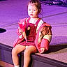 child, toddler, girl, sitting, stage, concert, music, musical_instruments, purple_lighting, colorful_jacket, overalls, sneakers, snack, popcorn, indoor, portrait, young_person, stage_lighting, performer_area, photograph